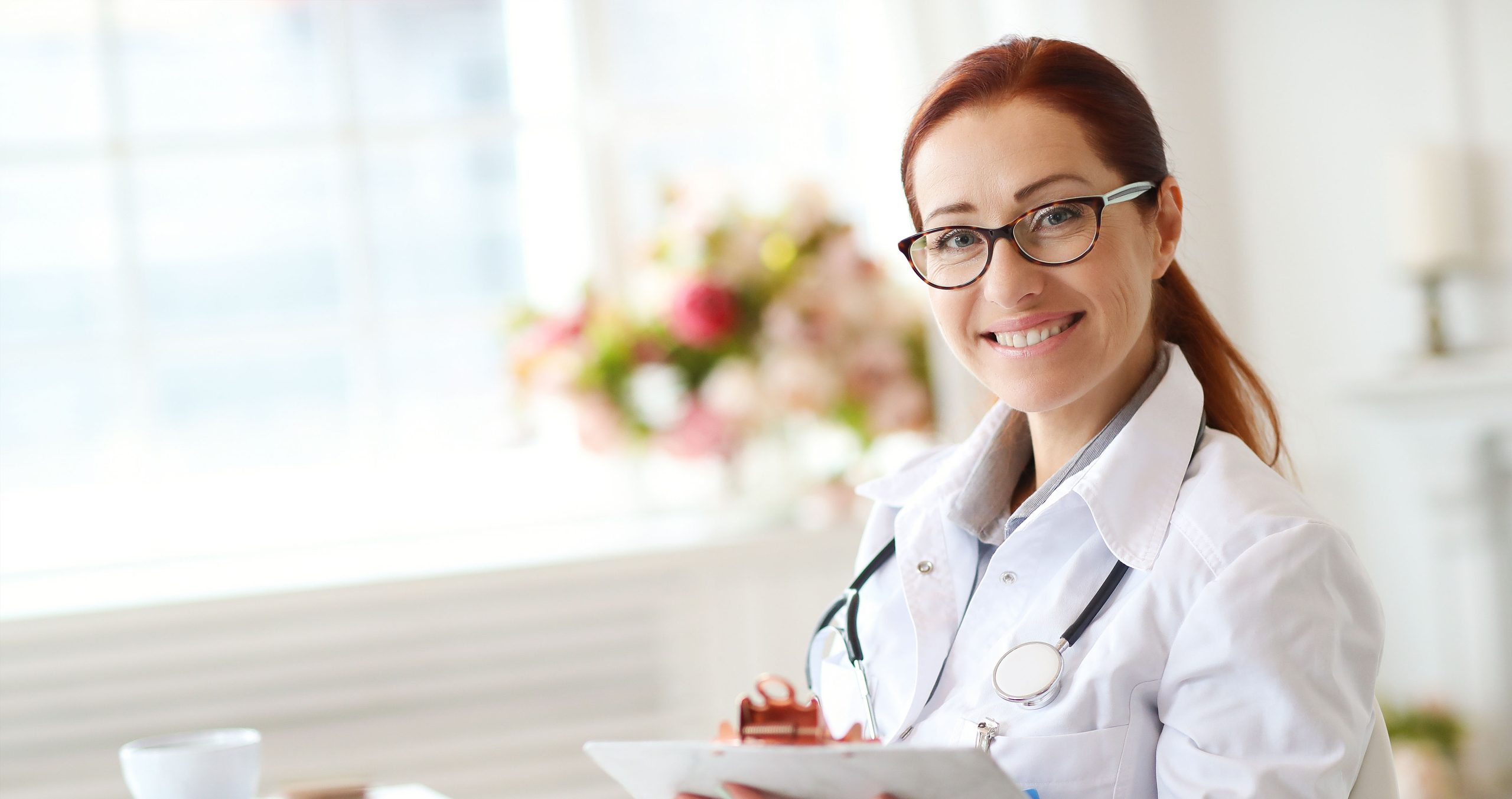 Woman medical professional in lab coat with stethoscope around neck and clipboard in hand
